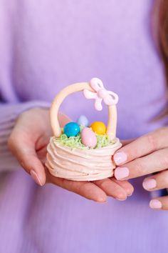 a woman is holding a small basket with eggs and candy in it while wearing pink nail polish