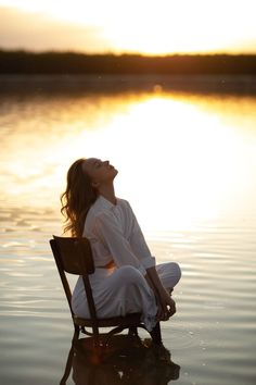 a woman sitting in a chair on top of a body of water with her eyes closed