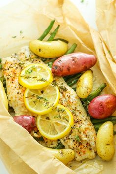 fish, potatoes and lemons on top of parchment paper with some herbs in the background