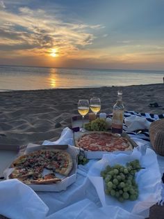 two pizzas and some wine on a table at the beach