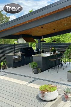 an outdoor kitchen and grill area with potted plants on the deck under a pergolated roof