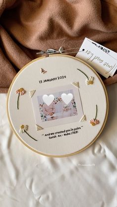 two hearts in the middle of a white frame on a bed with a tag attached to it