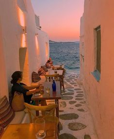 two people sitting at tables on the side of a building with water in the background