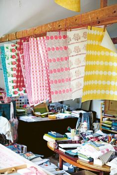 many different colored fabrics hanging from a wooden beam in a room with tables and chairs