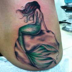 a woman with a green and black tattoo on her stomach sitting on top of a rock