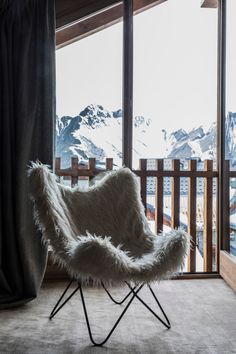 a white chair sitting in front of a window next to a snowy mountain covered hillside