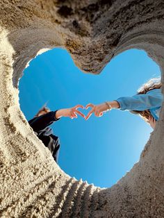 two people making a heart shape with their hands in the sand on a sunny day