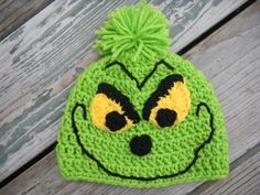 a crocheted green beanie with yellow eyes and a pom - pom