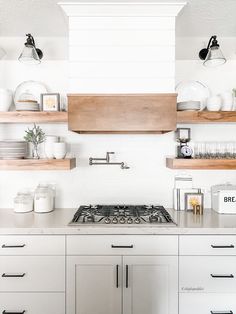 a kitchen with white cabinets and open shelving above the stove top is filled with dishes