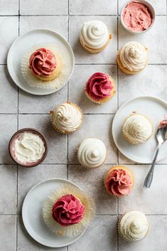 several cupcakes on white plates with pink frosting next to each other and spoon