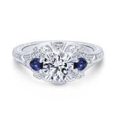 a white gold engagement ring with blue sapphire stones on the sides and an intricate filigree