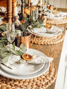 the table is set with plates, silverware and greenery on it's placemats