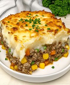 a white plate topped with a casserole covered in meat and veggies