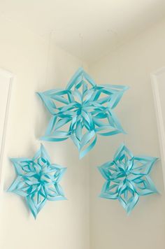 three blue paper snowflakes hanging from the ceiling in a room with white walls