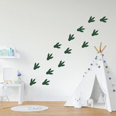 a teepee with green leaves flying in the air next to a white wall and wooden floor