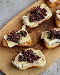 several pieces of bread with cheese and toppings on them sitting on a wooden platter