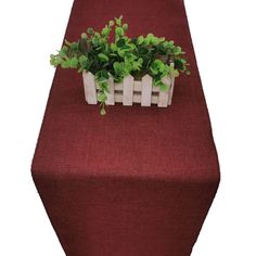 a planter with green plants in it on top of a red table cloth covered table