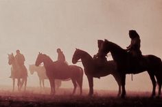 a group of people riding horses in the foggy field at sunset, with silhouettes of men and women on horseback