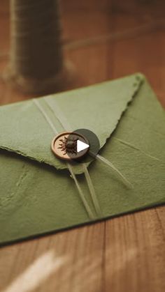 an envelope with a button on it sitting on top of a wooden table next to some thread