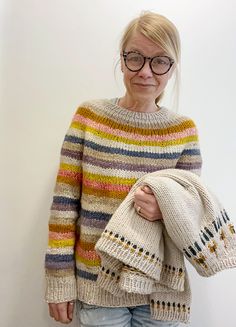 an older woman wearing glasses and holding a knitted sweater in front of a white wall