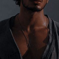 a young man wearing a necklace with a cross on it's neck, standing in front of a gray background