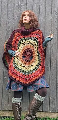 a woman wearing boots and a crocheted ponchy is standing in front of a wall