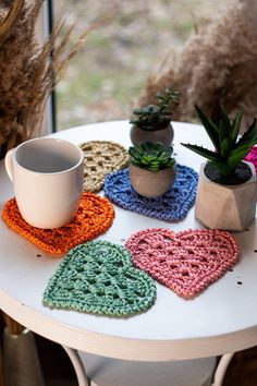 a table topped with potted plants and crocheted hearts on top of it