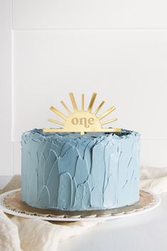 a blue cake sitting on top of a table next to a white plate with a gold one sign