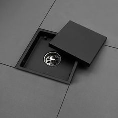 a square black box with two silver circles in it on a gray tile flooring area