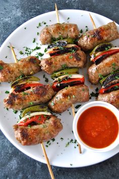 several skewered meats with vegetables and sauce on a white plate