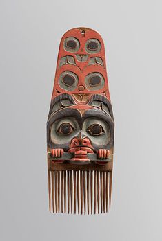 a red and black mask hanging from the side of a wooden comb with holes in it