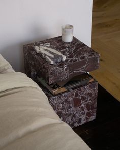 a marbled end table with a candle and books on it next to a bed