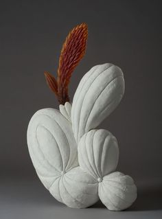 a white sculpture with an orange flower sticking out of it's back end, against a gray background