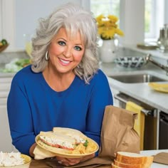 a woman sitting at a kitchen table holding a plate with sandwiches and bread on it