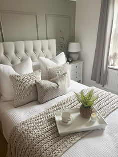 a tray with a cup and saucer sitting on top of a bed next to a window