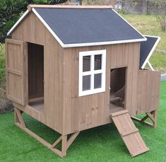 a small wooden house with a black roof and white windows on the grass in front of some trees