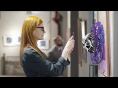 a woman is looking at an art piece on the wall and touching it with her hand