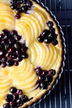 a pie sitting on top of a cooling rack covered in blueberries and custard