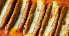 several sausages are lined up on top of a baking sheet with sauce and cheese