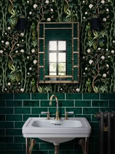 a bathroom sink sitting under a mirror next to a green tiled wall with leaves on it