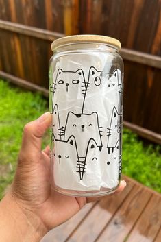 a person holding up a glass jar with cats on it in front of a wooden fence