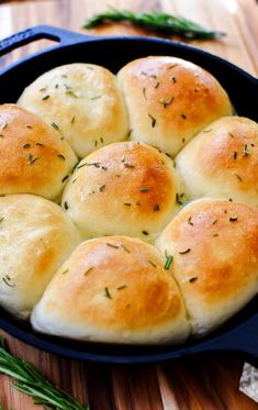 a pan filled with bread rolls on top of a wooden table next to green herbs