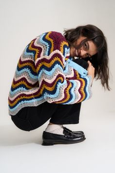 a woman squatting down while holding onto a crocheted blanket