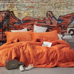 an orange comforter and pillows in front of a brick wall