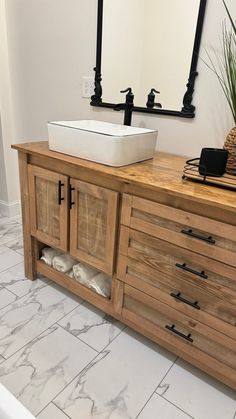 a bathroom sink sitting on top of a wooden cabinet next to a mirror and potted plant