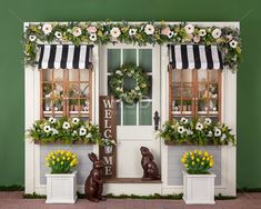 two bunny statues sitting in front of a window with wreaths and flowers on the windowsill