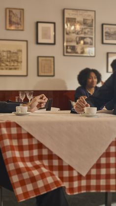 two people sitting at a table with cups and saucers in front of their faces