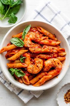 a white bowl filled with pasta covered in sauce and garnished with basil leaves