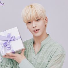 a man holding a white box with a purple bow on it's neck and wearing a green shirt