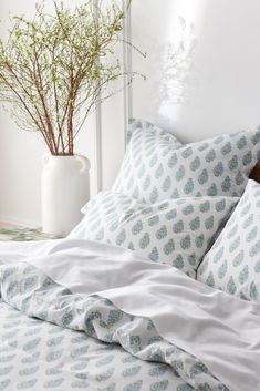 a bed with white sheets and blue flowers in a vase on the nightstand next to it